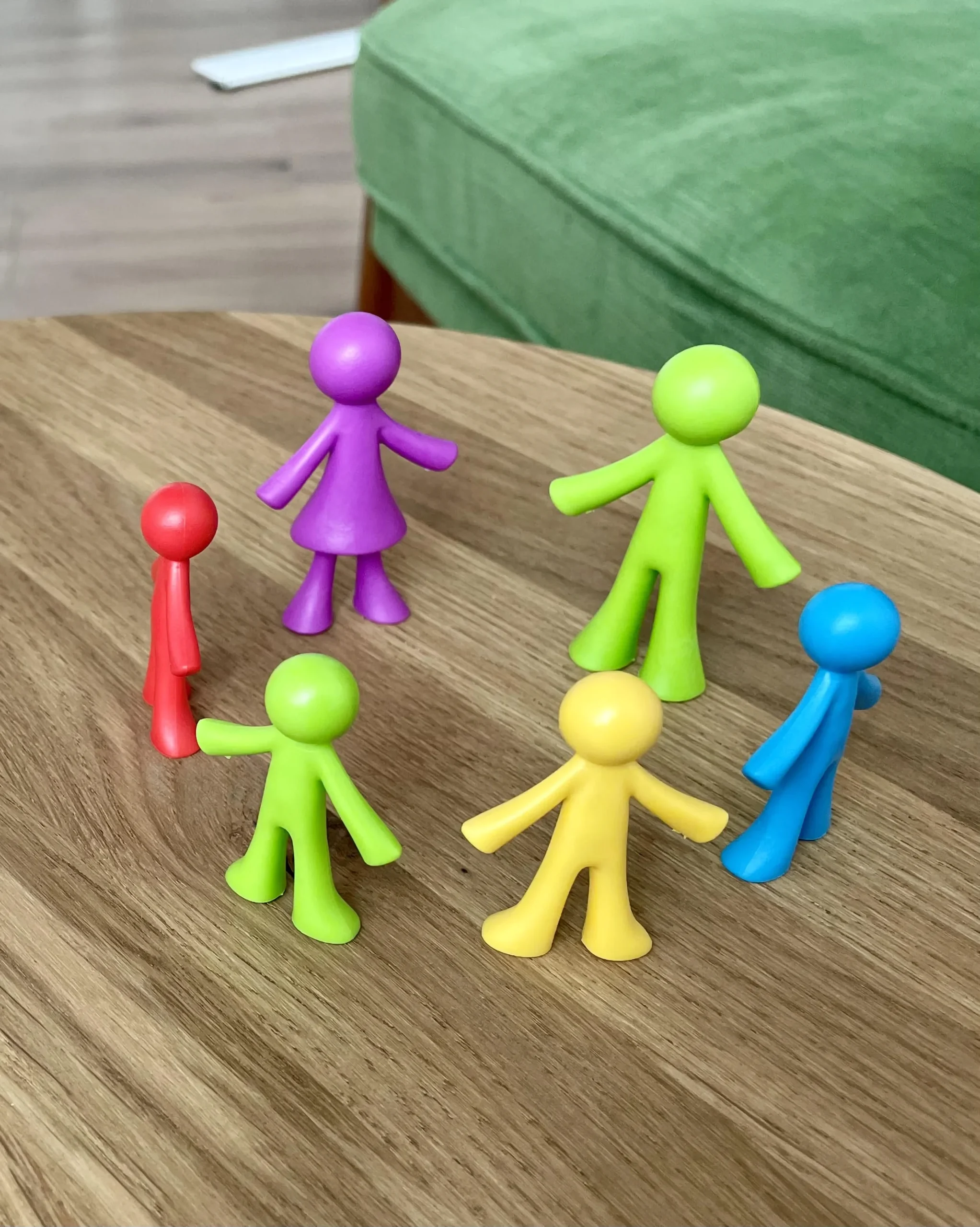 6 Farbige Figuren stehen im Kreis auf einem Holztisch und symbolisieren Zugehörigkeit und Zugehörigkeitsgefühl.
