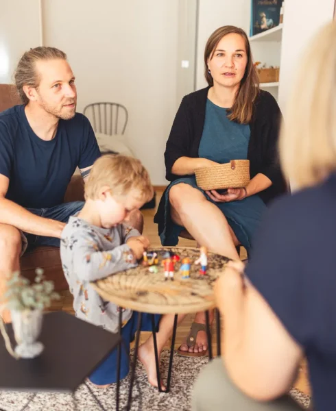 Thea Josi Stauber, psychologische Beraterin von Vertrauenswelt, über die Schulter hinweg, fotografiert mit Sicht auf eine junge Familie, welche die Familienberatung von Vertrauenswelt in Anspruch nimmt.