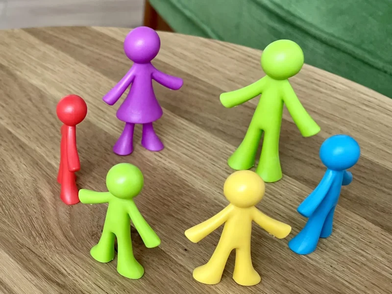 6 Farbige Figuren stehen im Kreis auf einem Holztisch und symbolisieren Zugehörigkeit und Zugehörigkeitsgefühl.